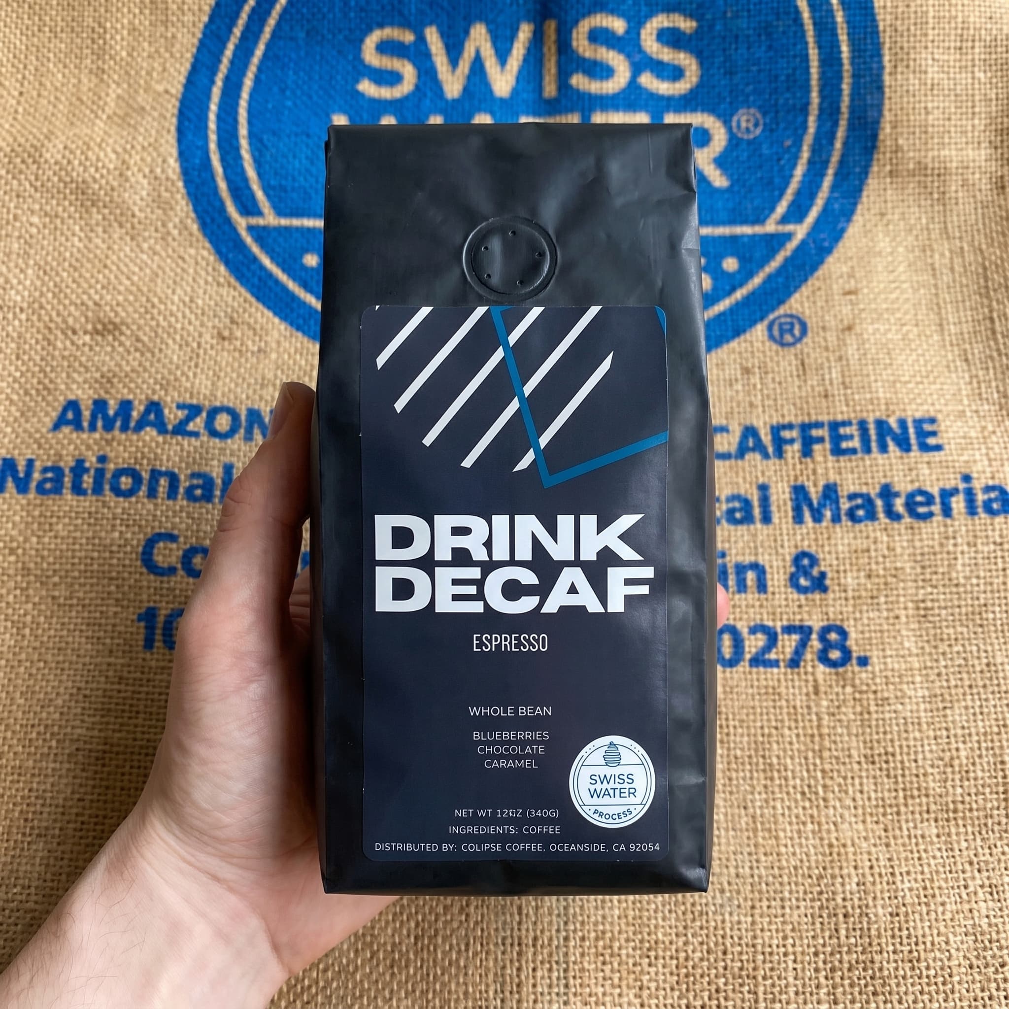 Drink Decaf espresso bag held in front of Swiss Water Process facility